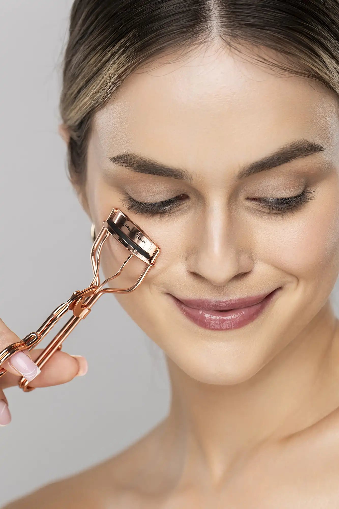 Woman curling her lashes with the QUALASH rose gold eyelash curler – profile view